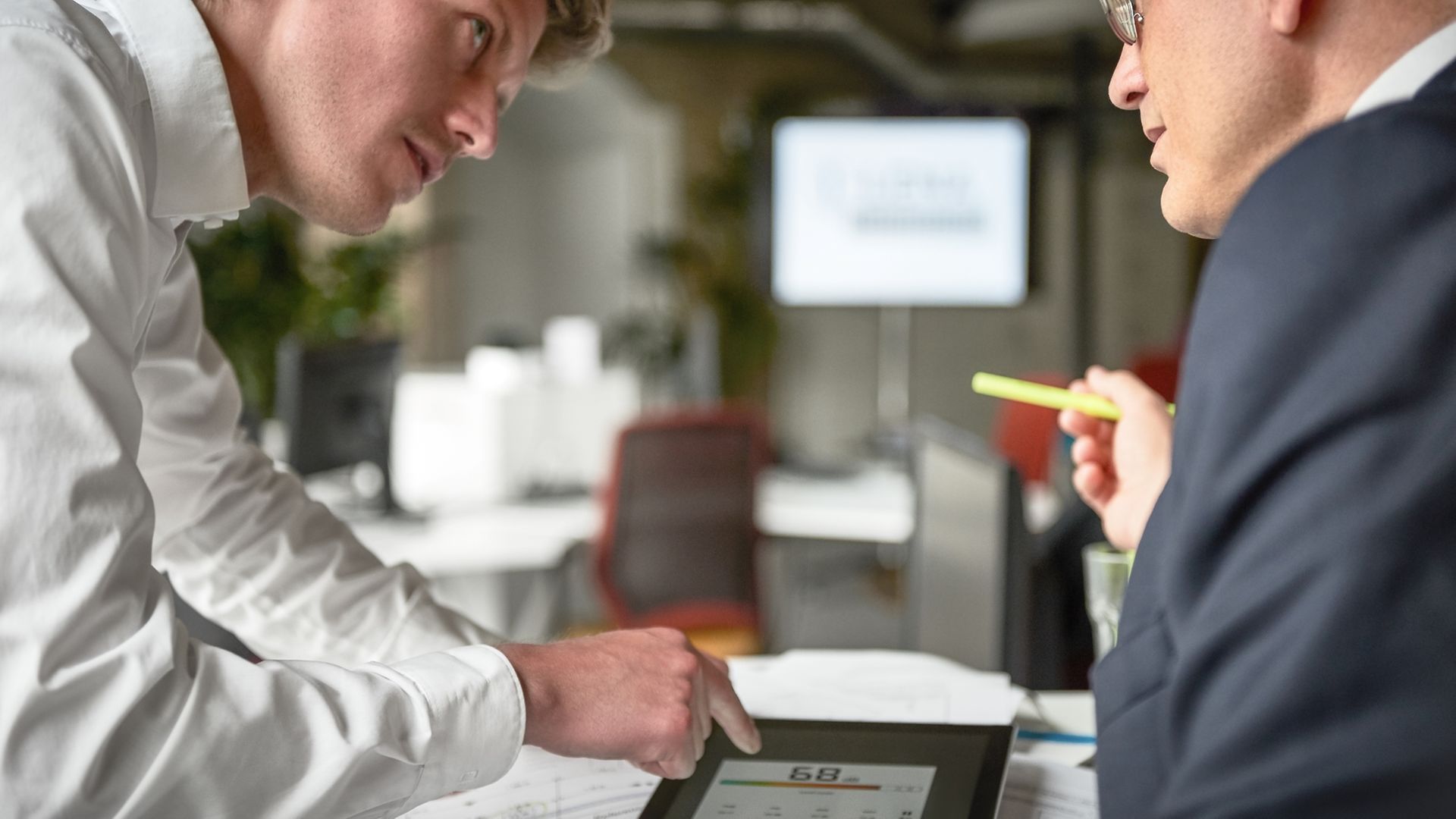 Zwei Mitarbeiter beraten über Ergebnisse, die auf einem Tablet gezeigt werden.