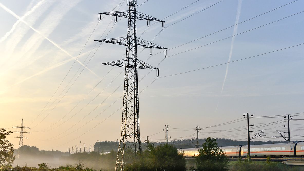 Ein Strommast steht neben einer Bahnstrecke auf einem Feld.