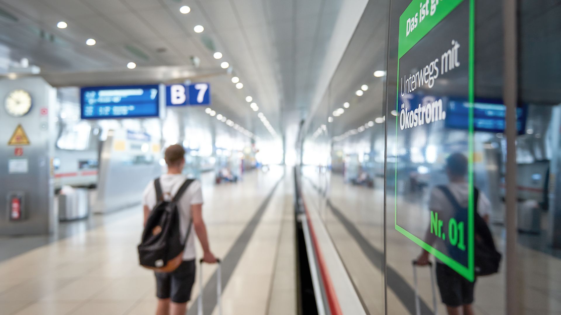 Ein Urlauber mit Rollkoffer ist an einem Bahngleis unterwegs.