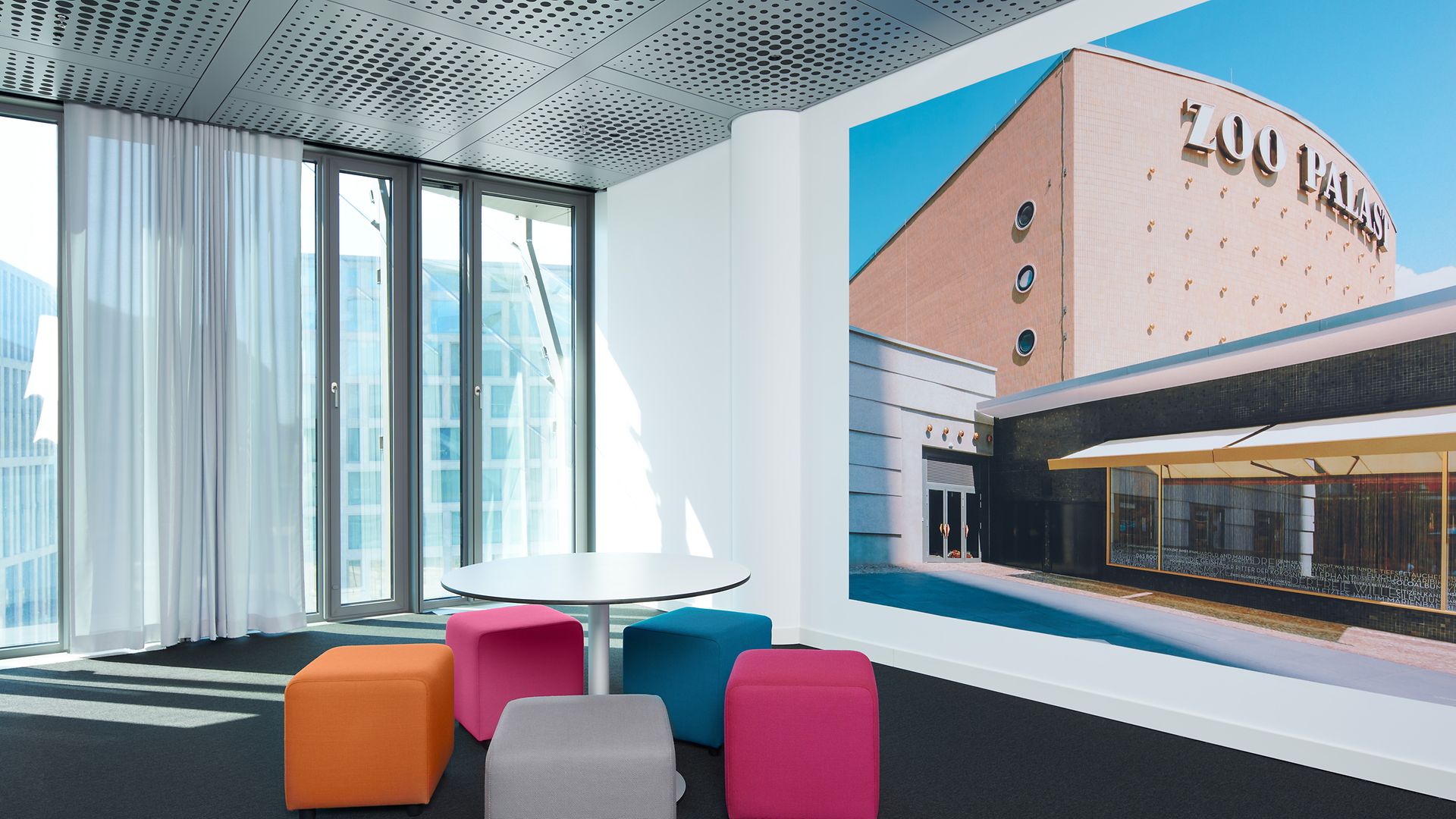 Eine Sitzgruppe mit bunten Hockern und einem großflächigen Wandbild