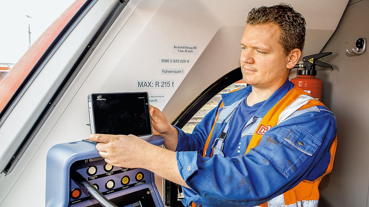 Ein Mann stellt in einem Führerhaus eines ICEs ein Display auf. 