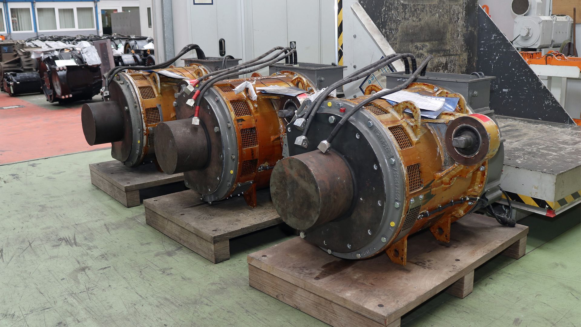 Drei alte Elektromotoren stehen auf Paletten gestapelt in einer Werkshalle.