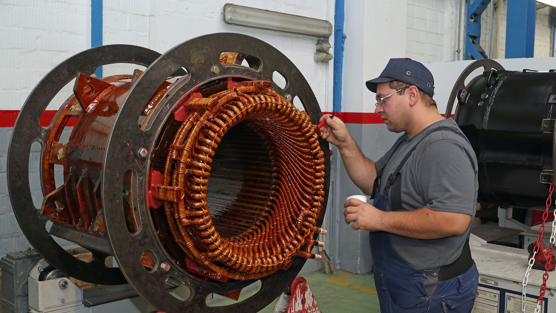 Ein Werksmitarbeiter trägt am Motorgehäuse mit einem Pinsel Isolierlack auf die Spulen des Elektromotors auf.