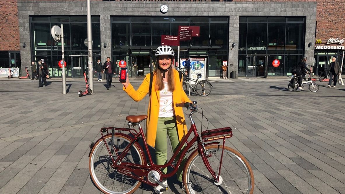 Eine Frau mit Fahrrad und Handy auf dem Vorplatz vom Bahnhof Hamburg-Bergedorf