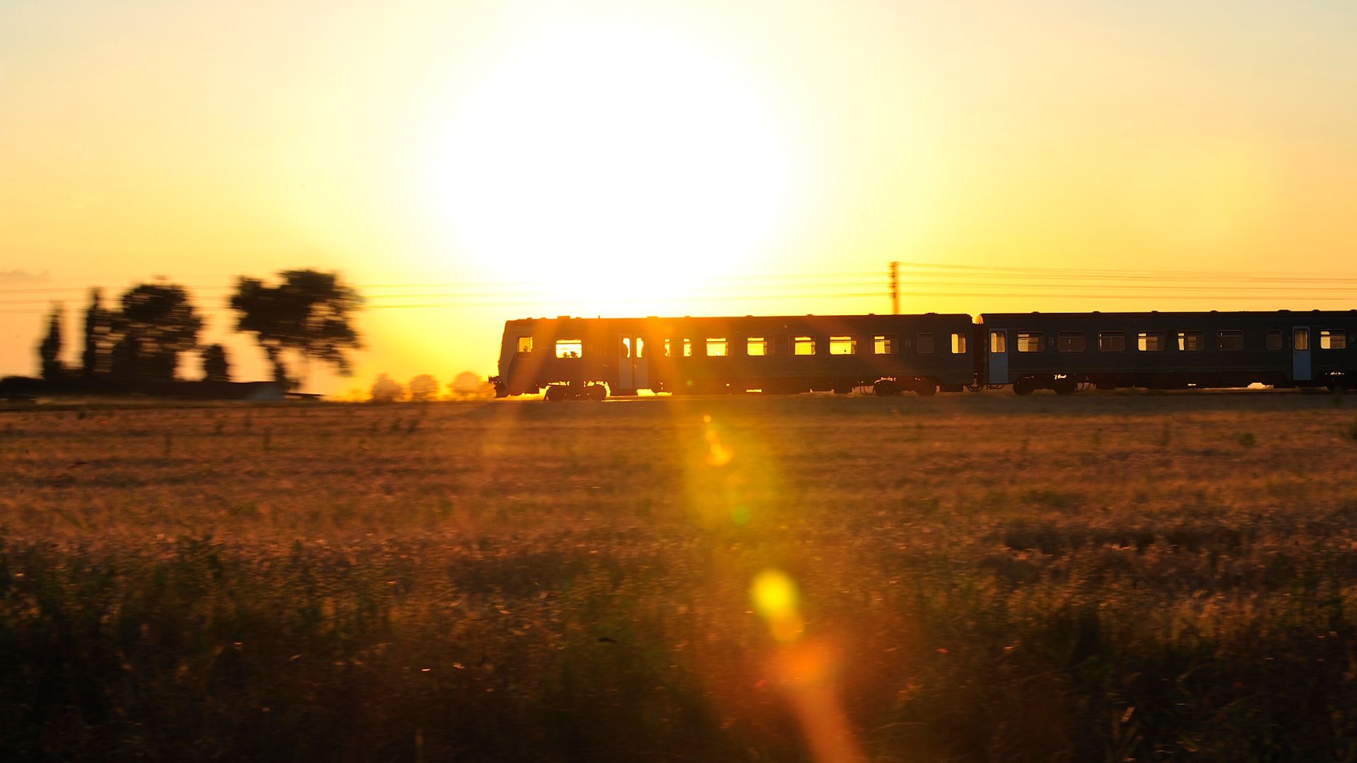 Ein Zug fährt durch die Landschaft, im Hintergrund die untergehende Abendsonne.
