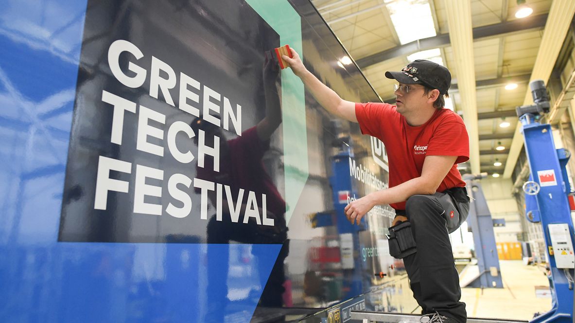 Ein Mann hängt ein Transparent auf mit dem Logo der GREENTECH-Messe. 