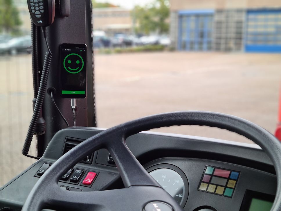 Blick auf das Lenkrad und Armaturenbrett eines Fahrzeugs, daneben ein Handy mit grünem Smiley auf dem Display.