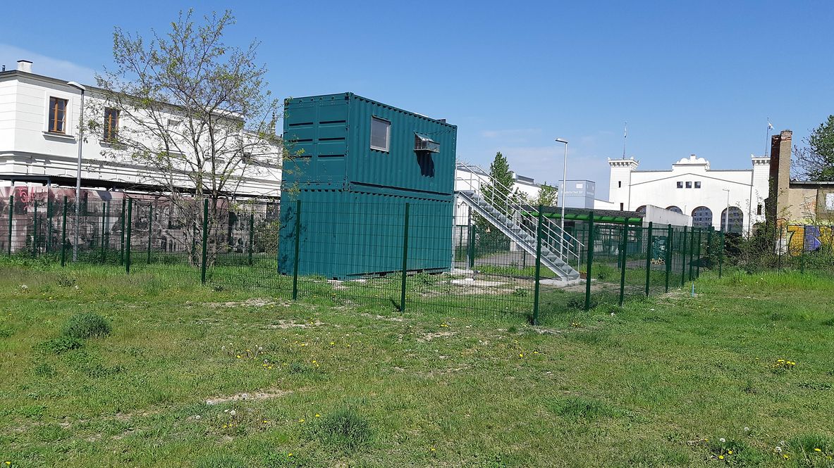 Ein doppelstöckiger Container als Taubenschlag steht auf einem eingezäunten Teil einer Wiese