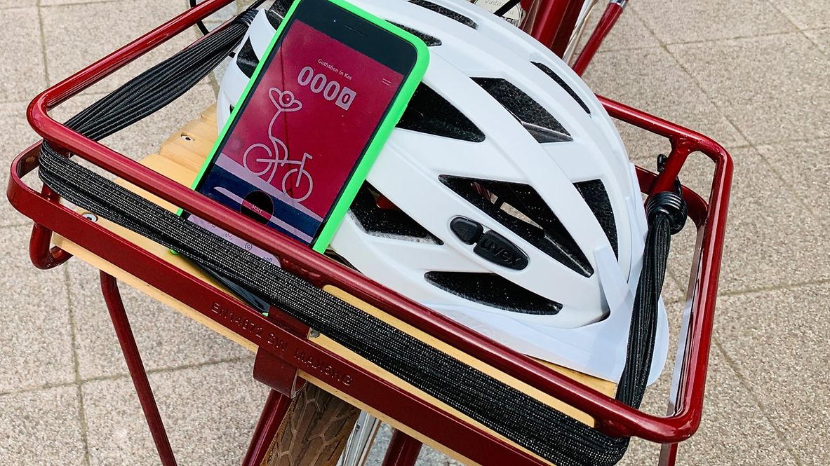 Fahrradkorb mit einem Helm und einem Smartphone, mit der geöffneten Rad+ App 