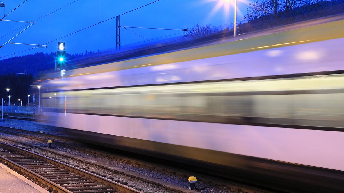 Ein Zug fährt auf einer Schiene vorbei und ist nur schemenhaft zu sehen.