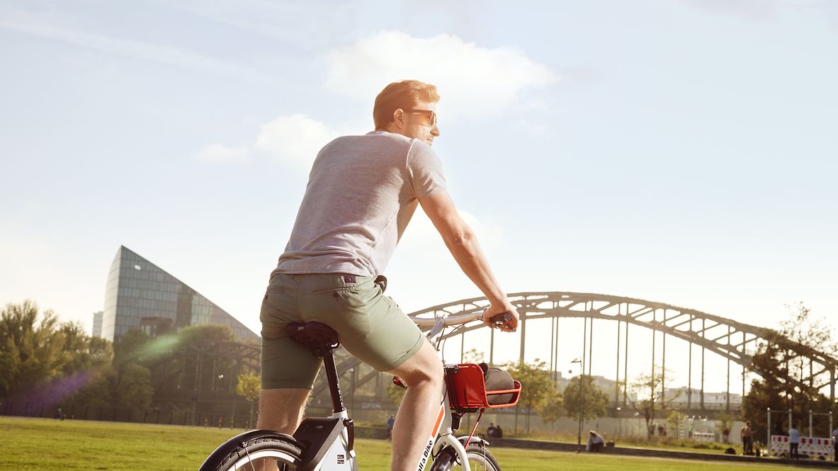 Ein Mann fährt mit dem Rad durch einen Park und schaut in die Sonne.