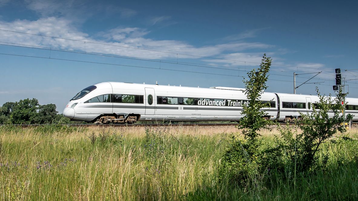 Ein ICE mit der Aufschrift advanced TrainLab fährt durch eine grüne Landschaft. 
