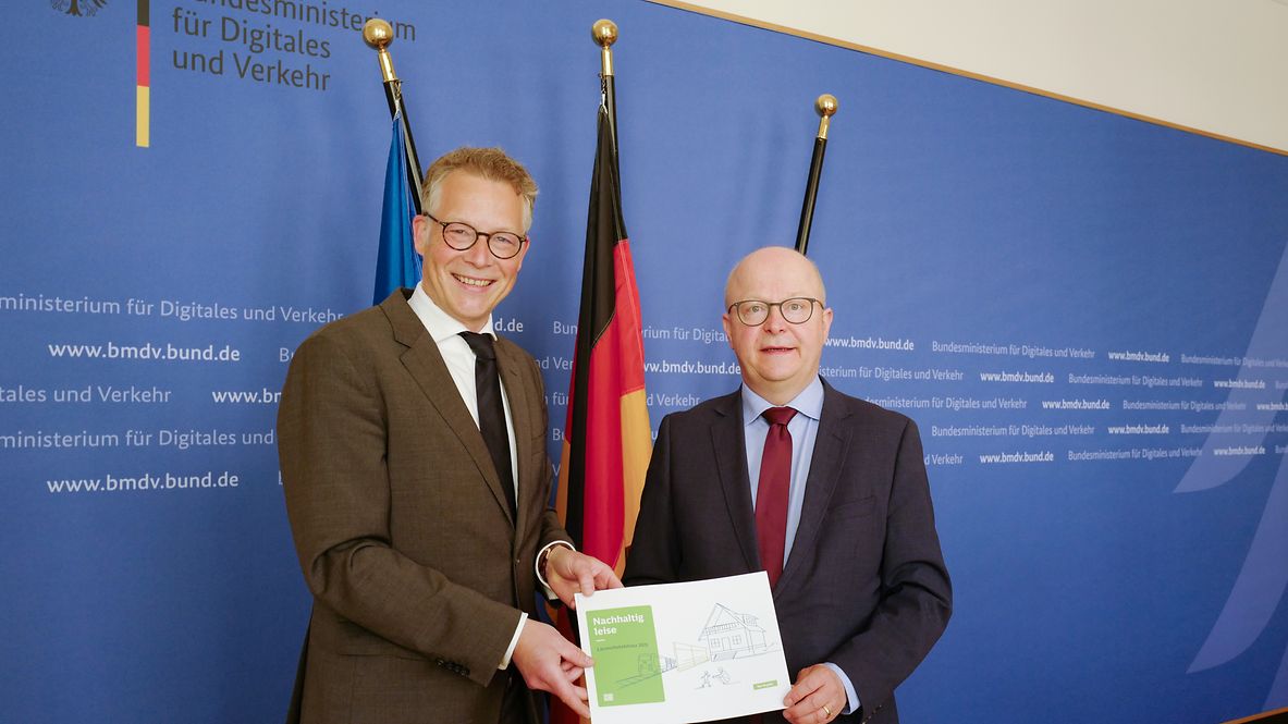 Ein Bahnvertreter übergibt des Lärmschutzbericht 2021 an einen Politiker.