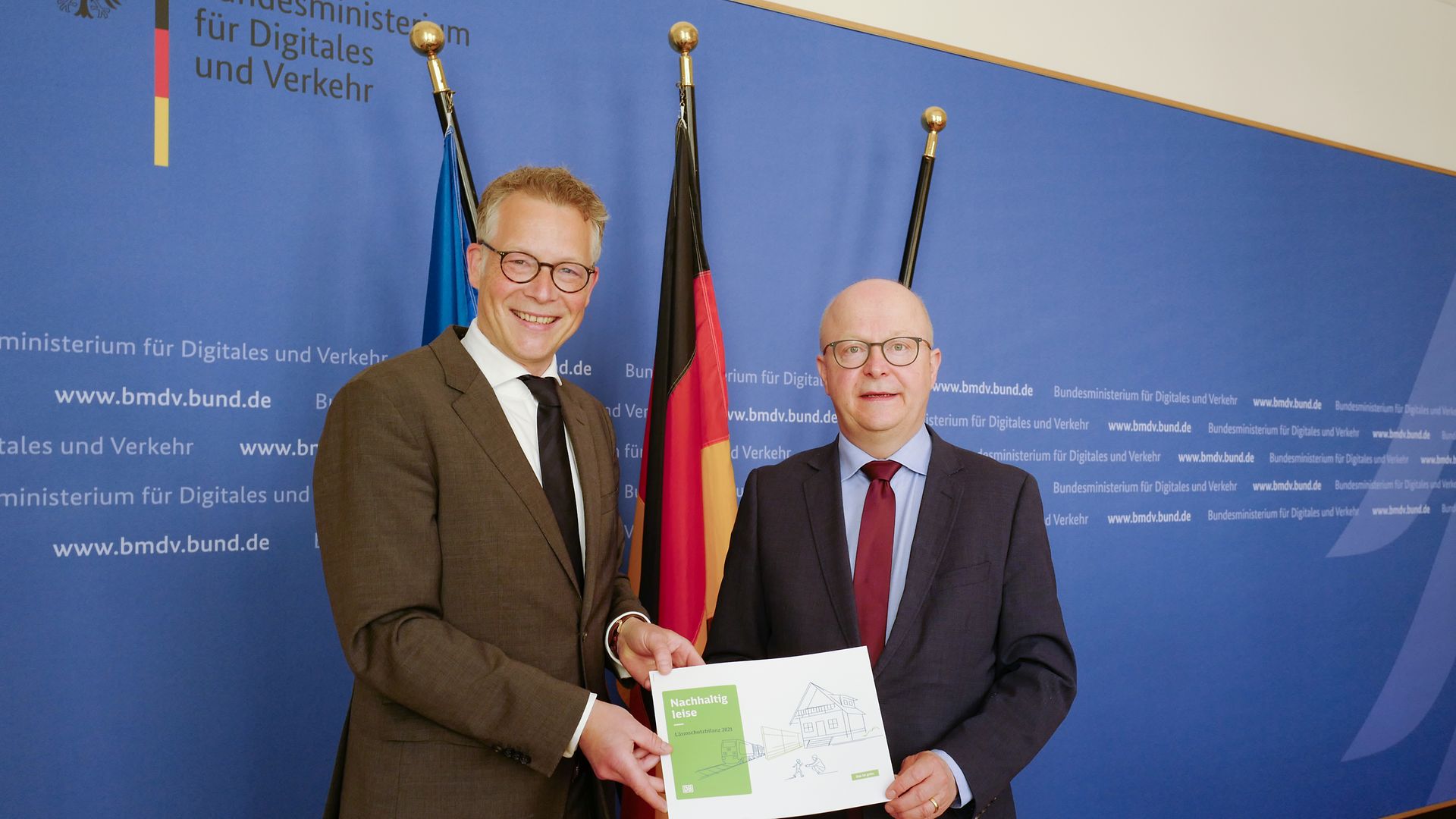 Ein Bahnvertreter übergibt des Lärmschutzbericht 2021 an einen Politiker.