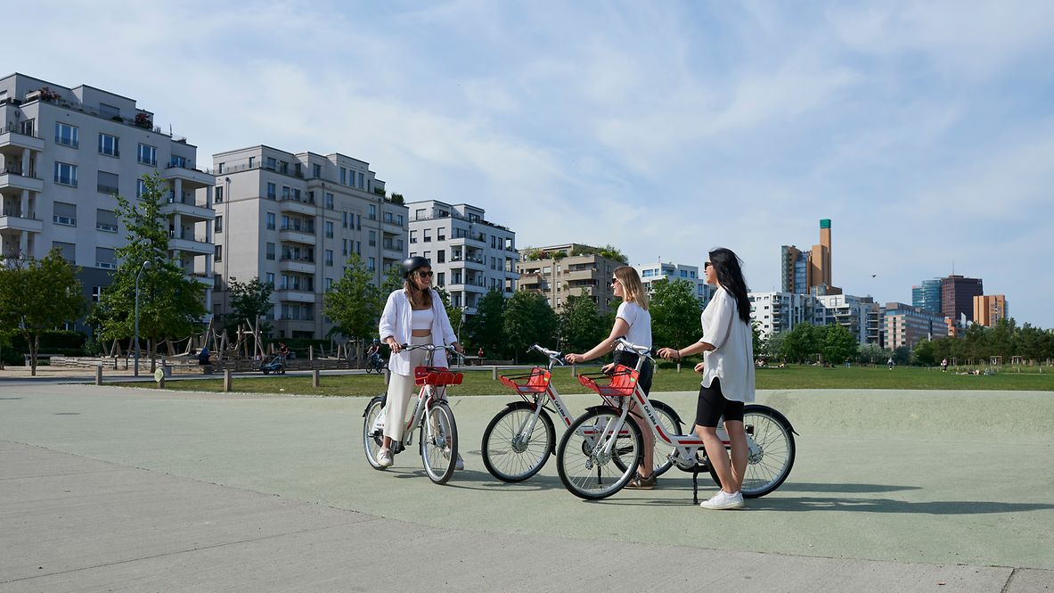 Drei Frauen begrüßen sich in einem Park, jede hat ein Fahrrad der Call a Bike-Initiative dabei.