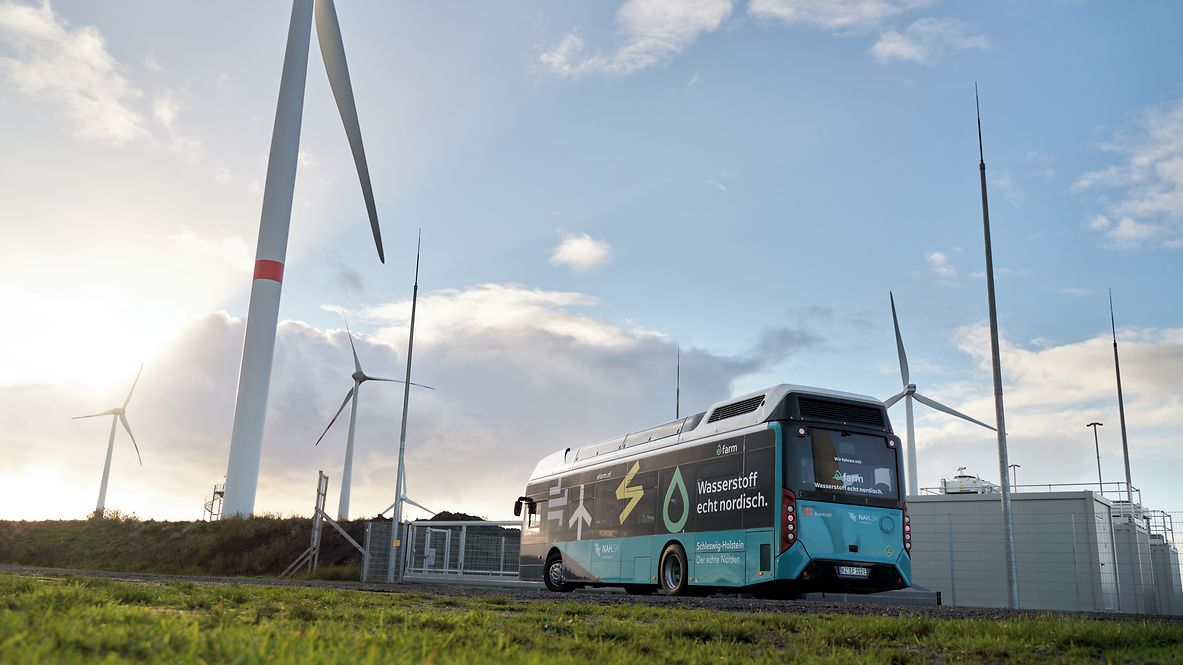 Blau-weißer Wasserstoffbus steht zwischen Windrädern