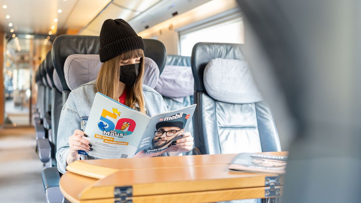 Reisende mit FFP-2 Maske liest DB mobil