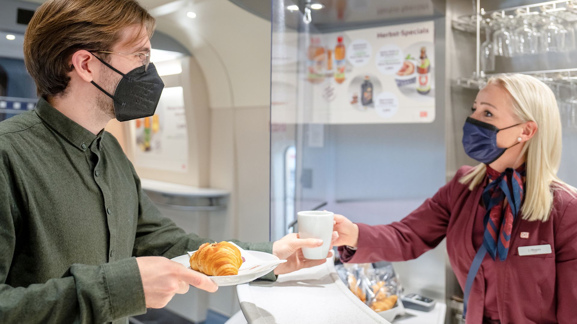 Eine Mitarbeiterin des Bordbistros serviert einem Bahnkunden seine Bestellung auf Porzellangeschirr