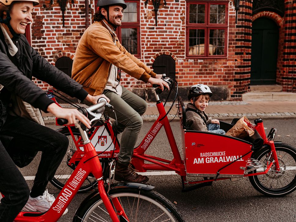 Ein Mann fährt ein Lastenpedelec von StadtRad Lüneburg. Im vorderen Lastenkorb sitzt ein Kind.