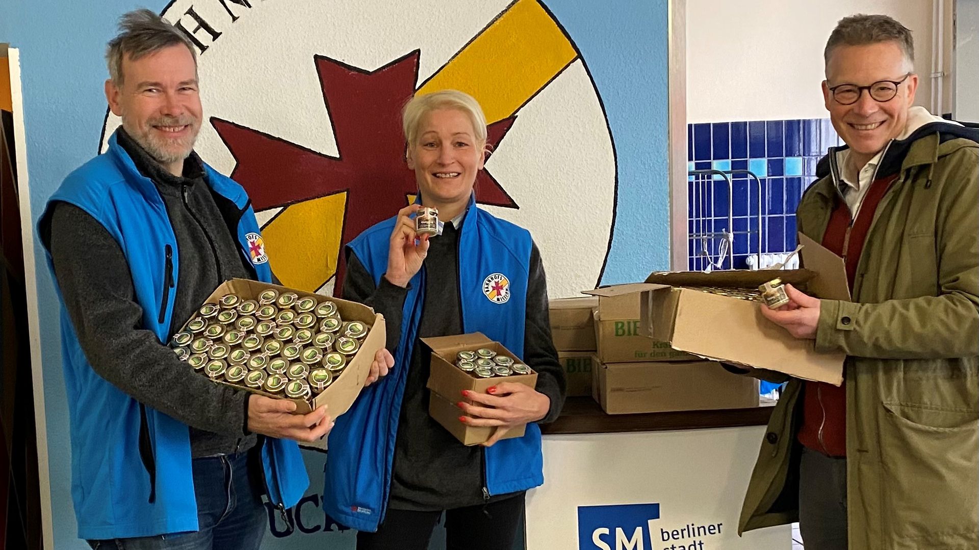 Ein Vertreter der Deutschen Bahn überreicht mehrere Kartons Gleisgoldhonig an Mitarbeitende der Bahnhofsmission.