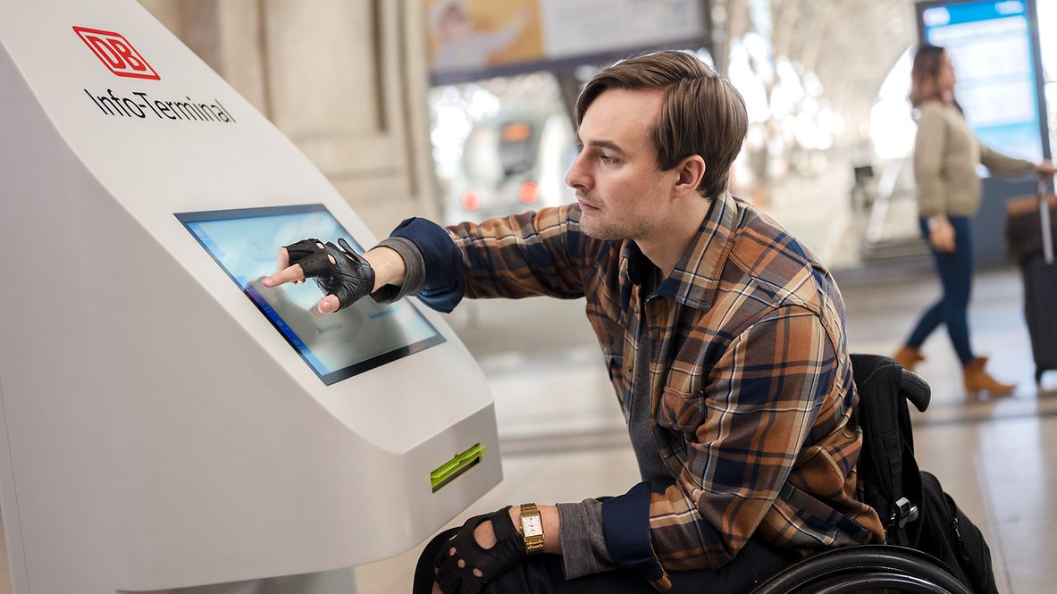 Ein Rollstuhlfahrer an einem DB Info-Terminal in der Bahnhofshalle des Hauptbahnhofs Leipzig.