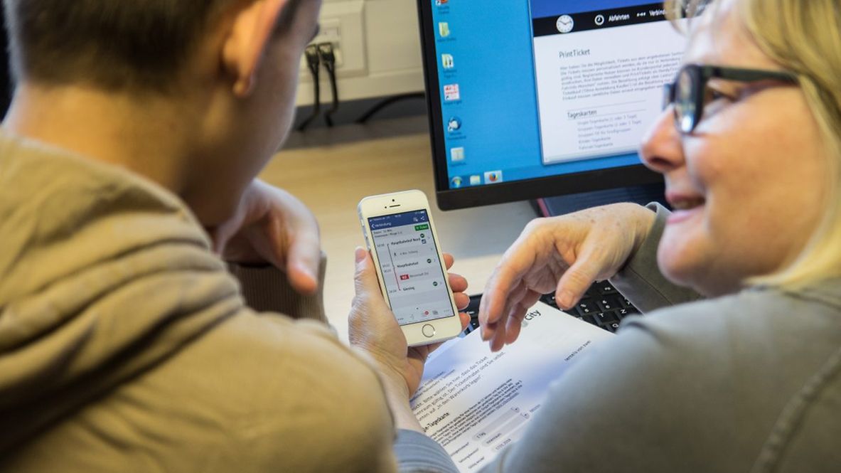 Ein junger Mann und eine ältere Frau beugen sich über ein Smartphone.