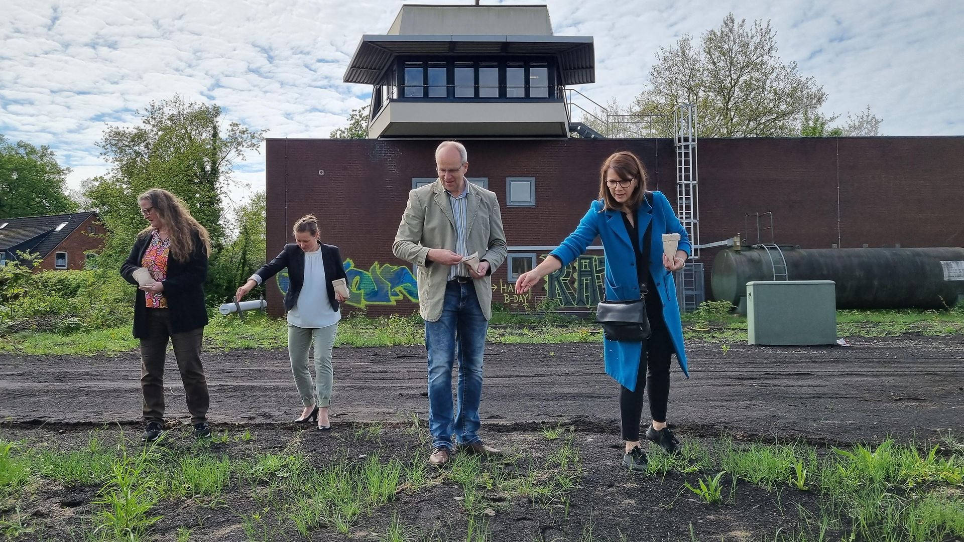 DB-Mitarbeitende verteilen Saatgut auf einem Gelände mit stillgelegten Gleisen.