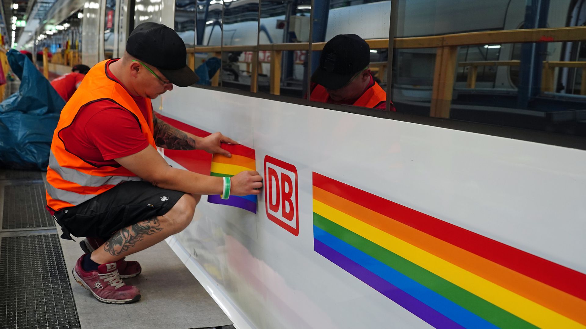 Ein Mann beklebt einen ICE mit einem Regenbogenstreifen.