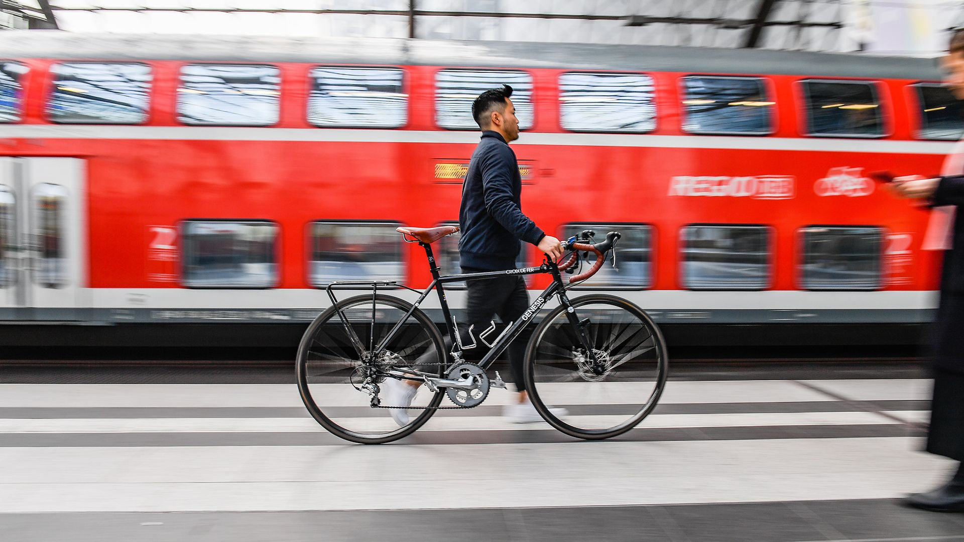 Ein Mann schiebt ein Fahrrad an einem Bahnsteig.