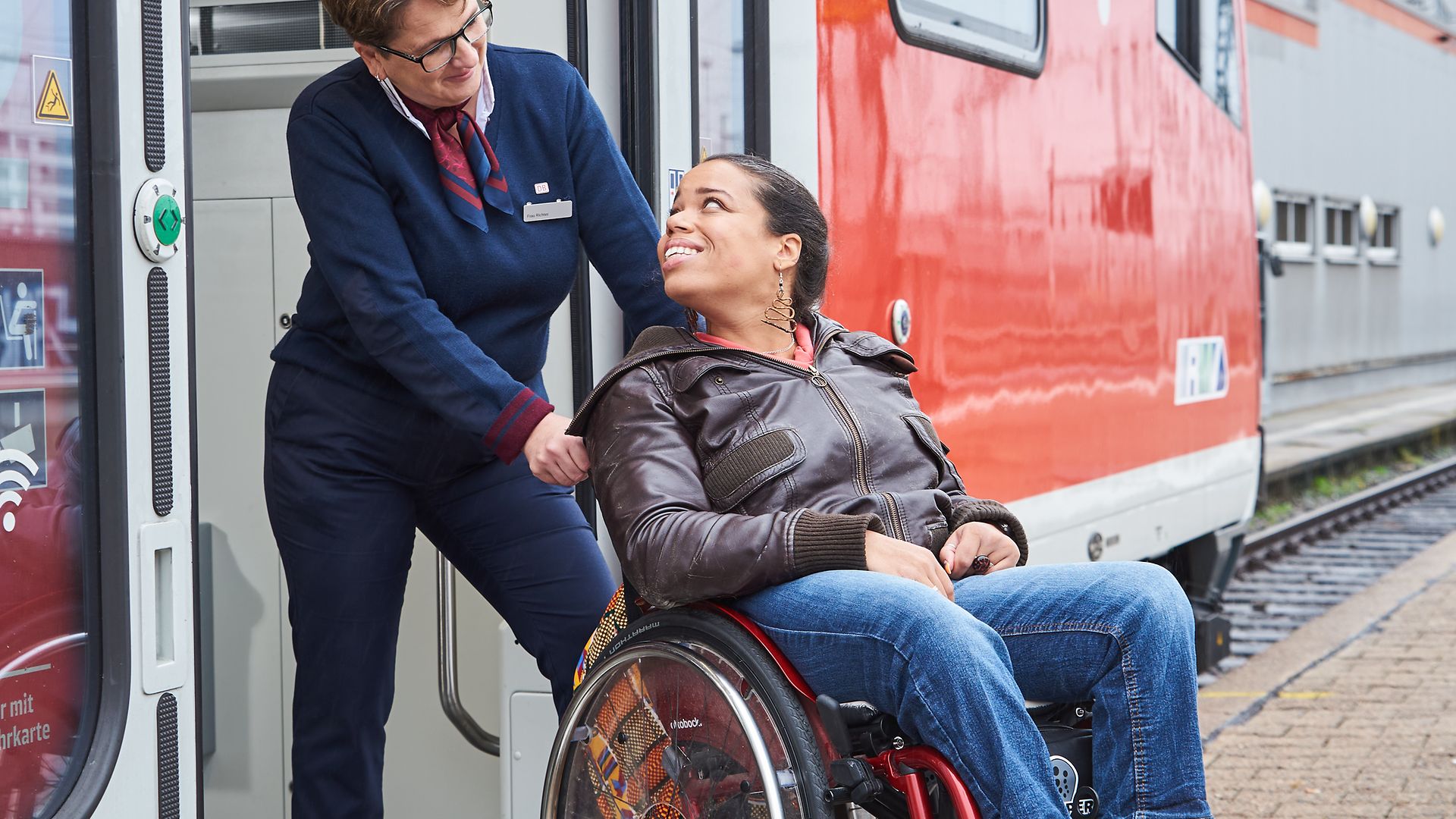 Eine Zugbegleiterin hilft einer Frau im Rollstuhl beim Einstieg in einen Regionalzug.