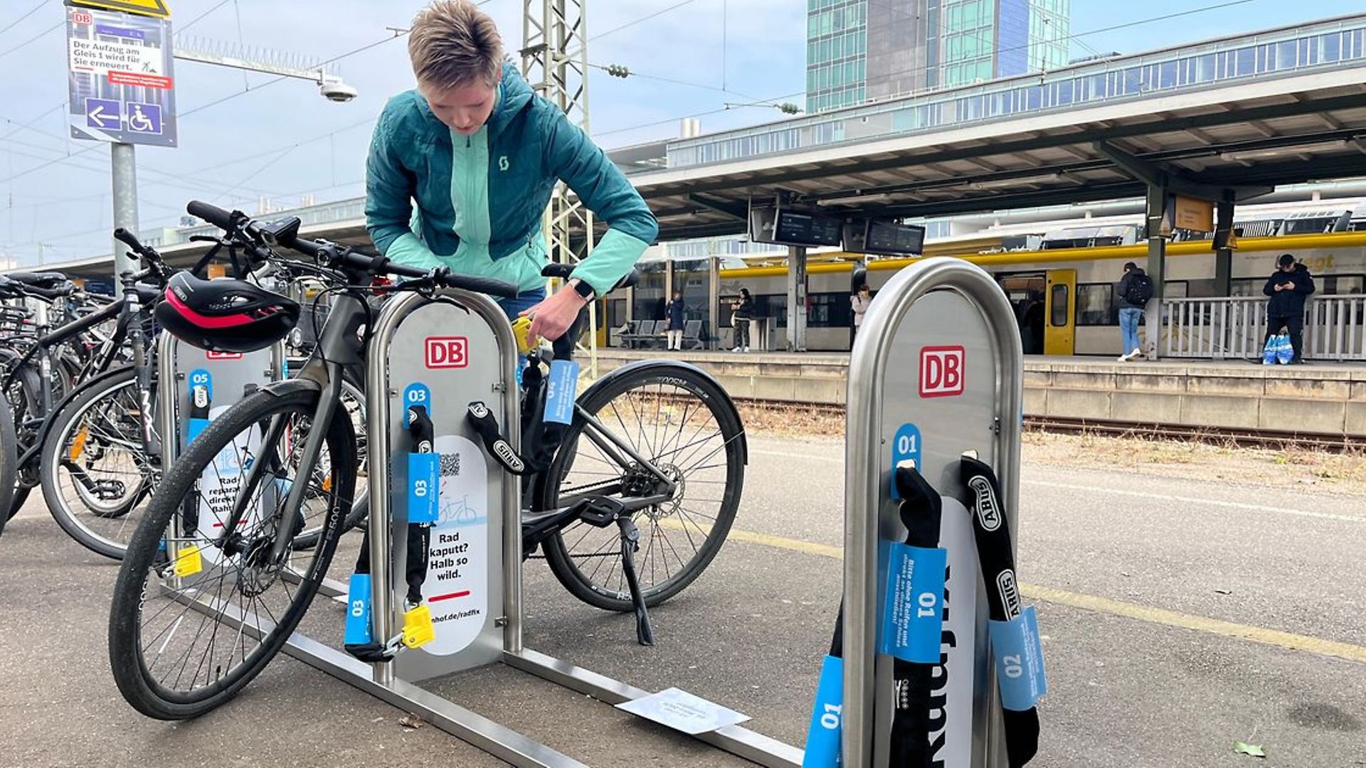 Eine Frau schließt ihr Fahrrad am Bahnhof an einem Stellplatz von DB Radfix an. 