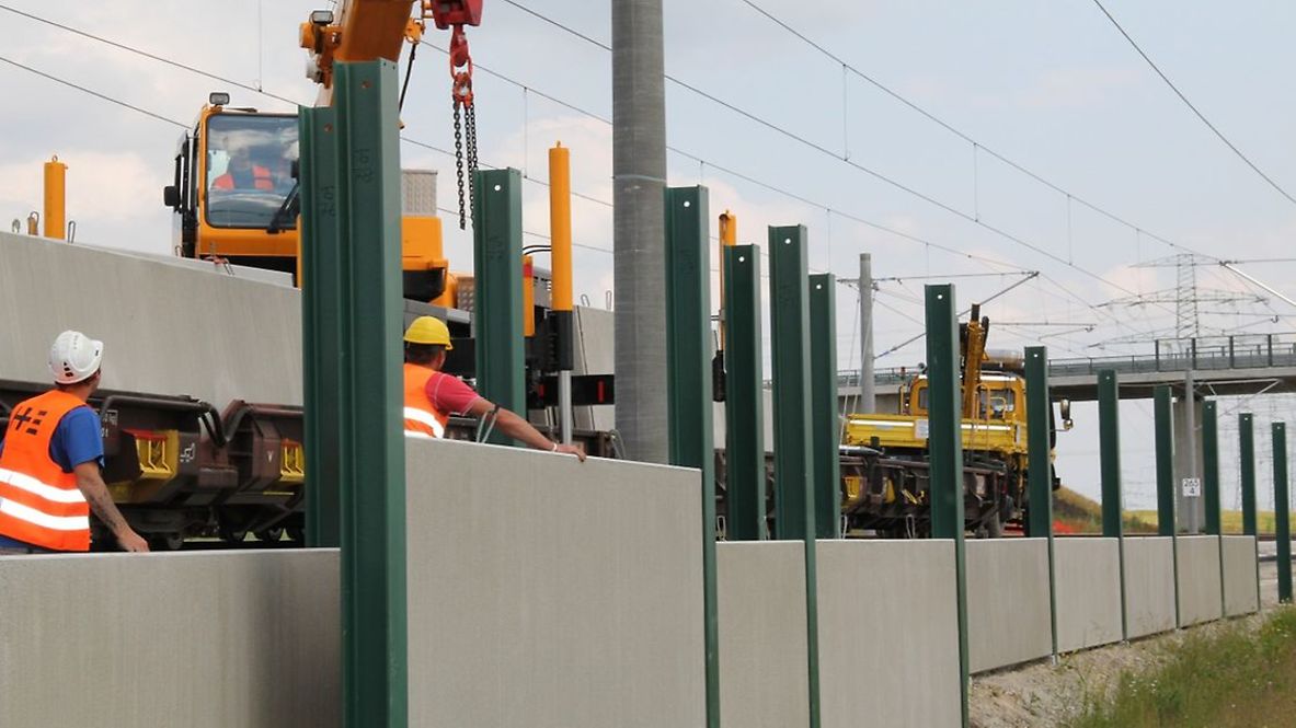 Bauarbeiter errichten Lärmschutzwände an einer Bahnstrecke.