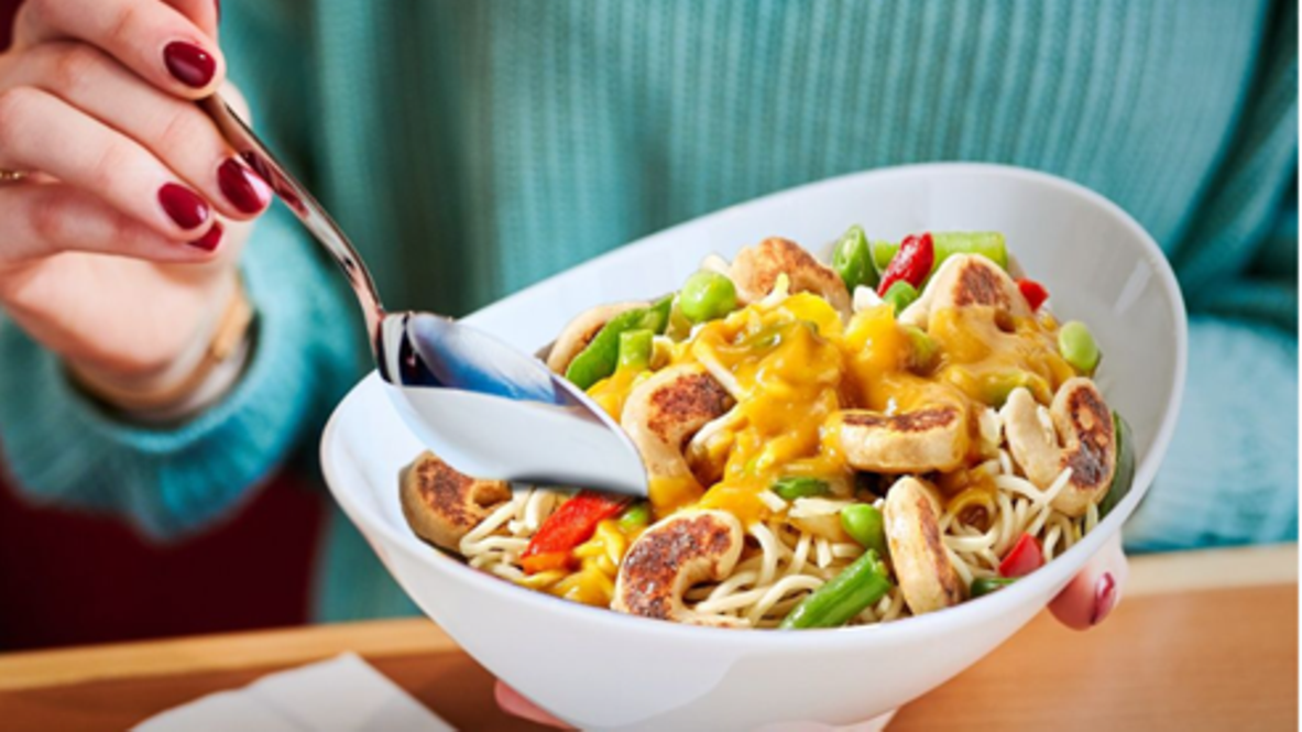 Eine Person isst eine vegane Wokpfanne mit rein pflanzlichen Garnelen