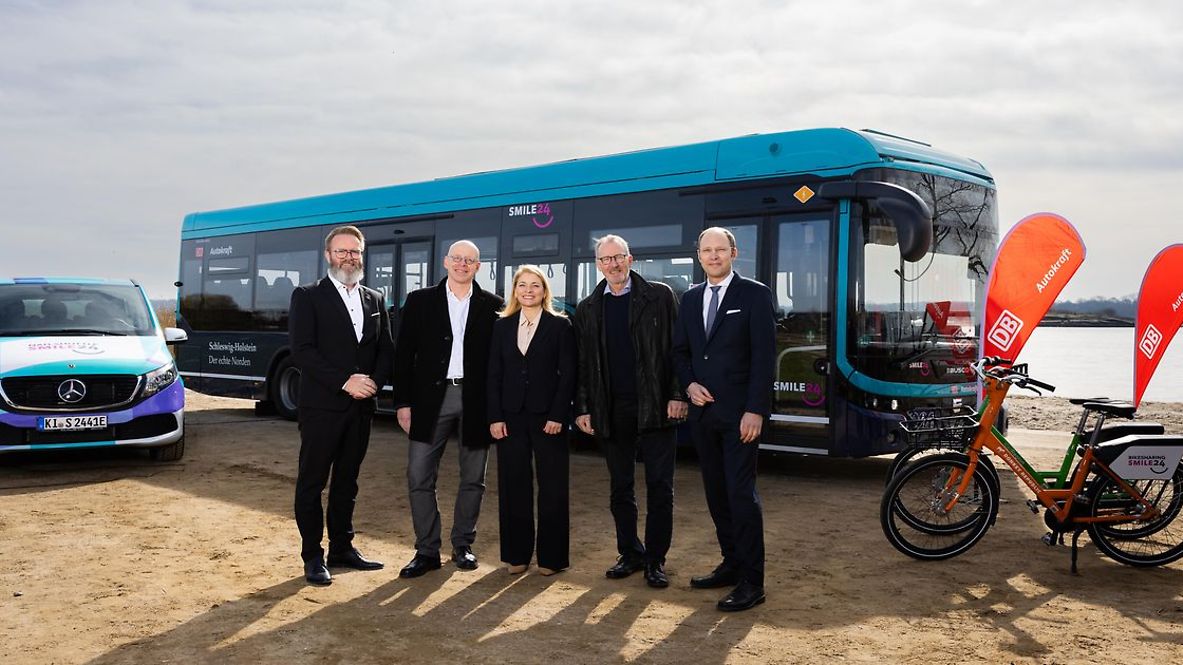 Vier Männer und eine Frau posieren für ein Gruppenbild vor einem blauen Elektrobus.