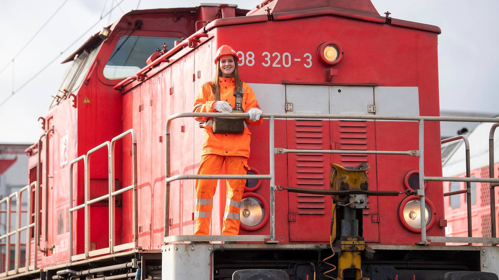 Eine junge DB Mitarbeiterin steht vor einer Lok.