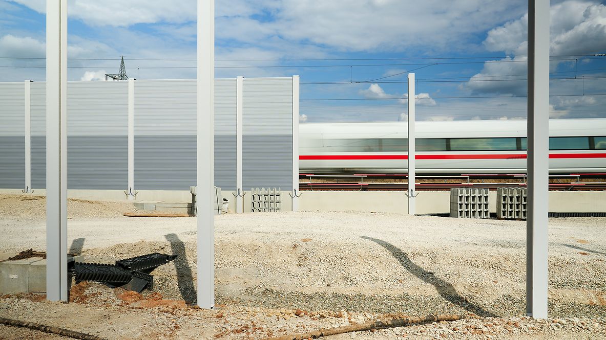 Eine Baustelle zur Errichtung einer Lärmschutzwand, im Hintergrund fährt ein ICE vorbei.
