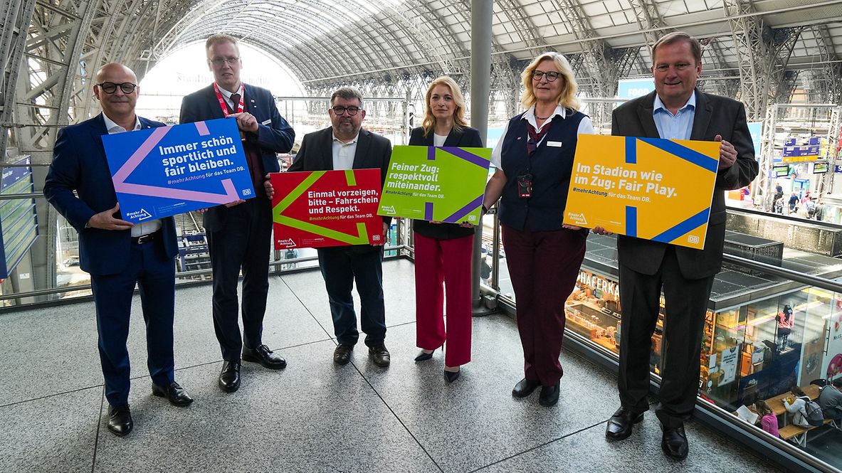 Sechs DB-Mitarbeitende stehen im Bahnhof und halten Schilder der Aktion #mehrAchtung hoch