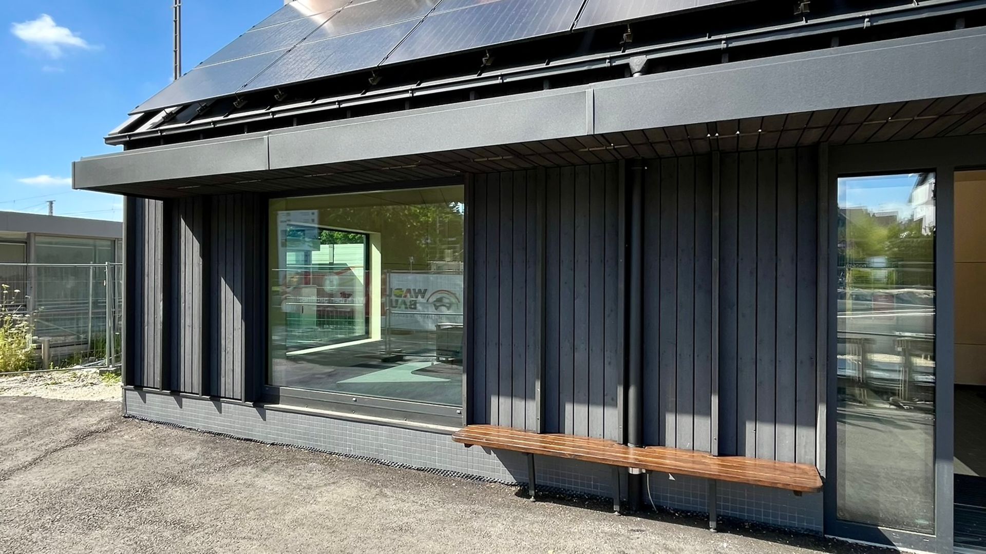 Vorderansicht des Bahnhofsgebäudes in Zorneding mit großen Fensterflächen und Sitzbank.