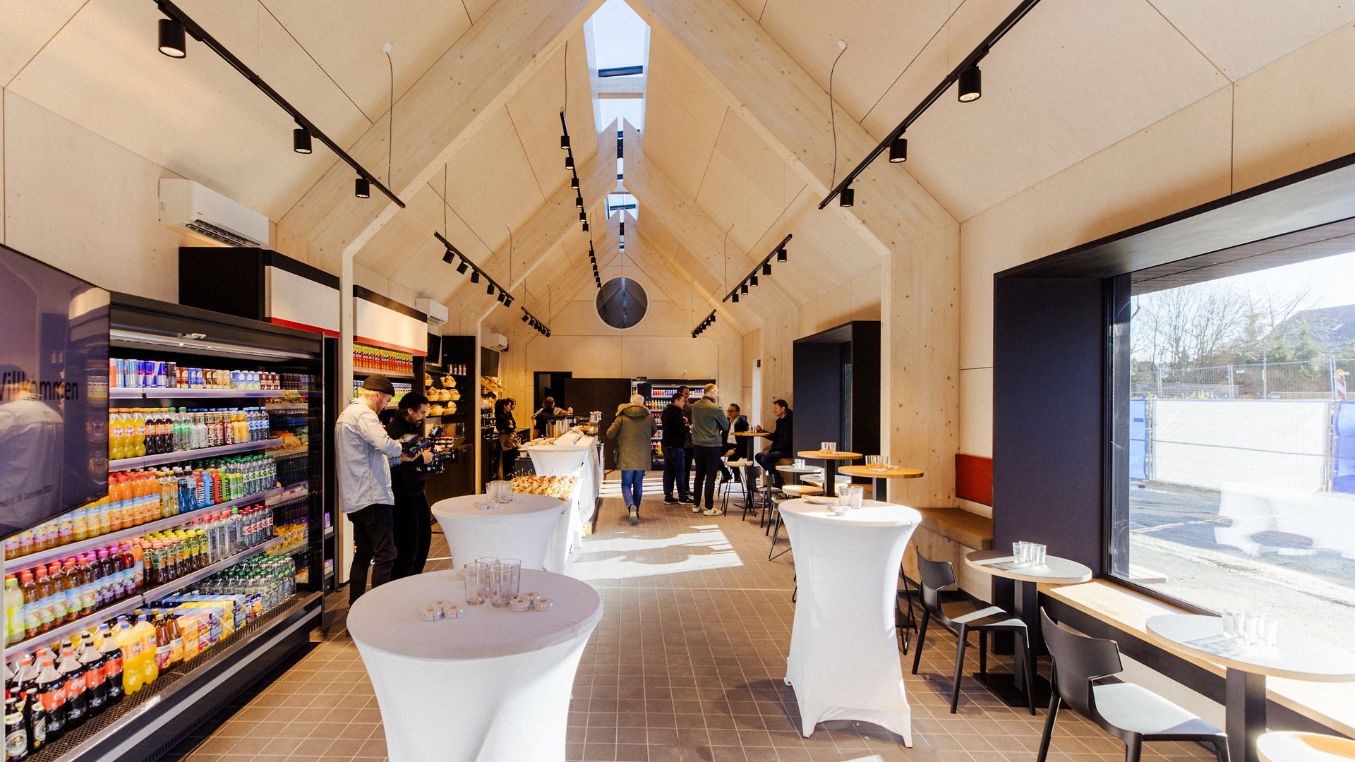 Blick in das Empfangsgebäude in Zorneding mit Verkaufsregalen, Stehtischen und Menschen im Hintergrund.