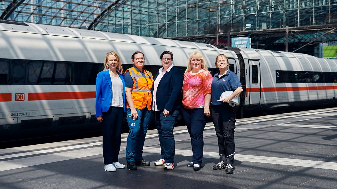 Fünf DB-Mitarbeiterinnen aus verschiedenen Berufsgruppen stehen vor einem ICE.