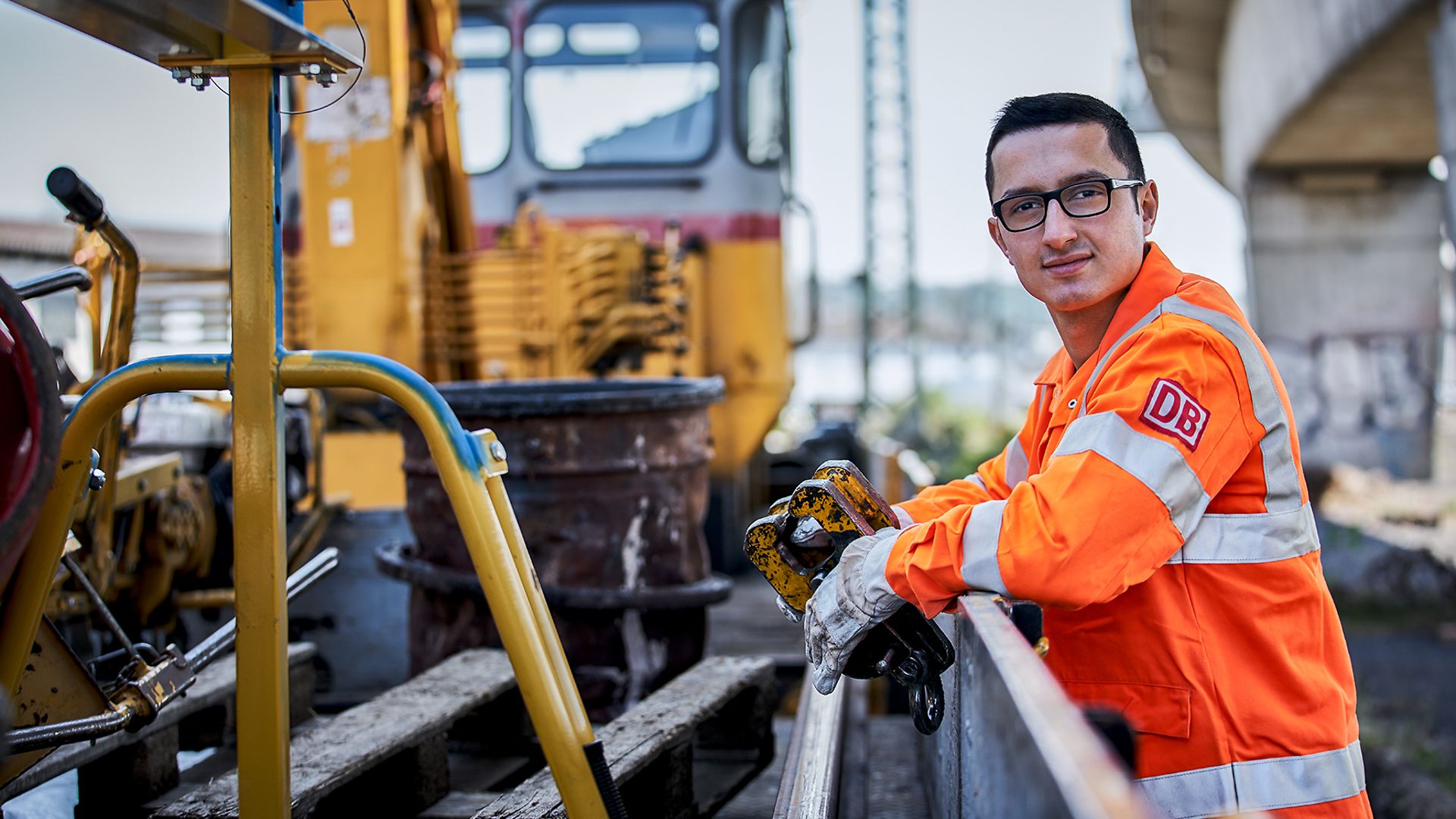 Ein junger Mann auf einer Baustelle an den Gleisen schaut in die Kamera.