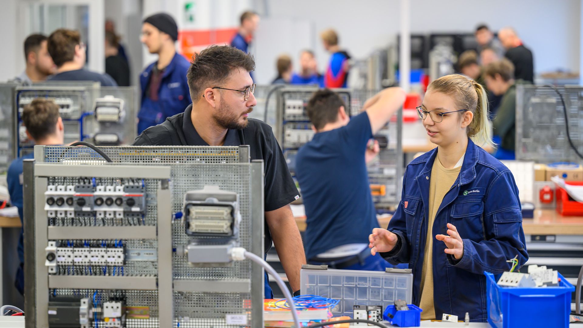 Ein Ausbilder der DB und eine Auszubildende sprechen miteinander in einer Werkstatt.