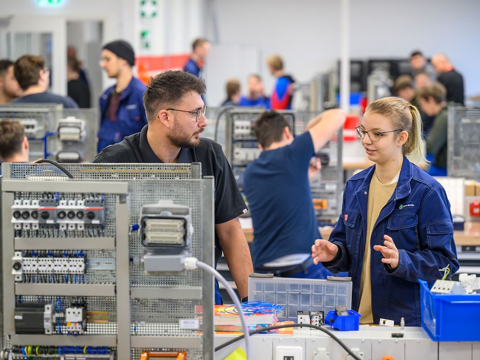 Ein Ausbilder der DB und eine Auszubildende sprechen miteinander in einer Werkstatt.