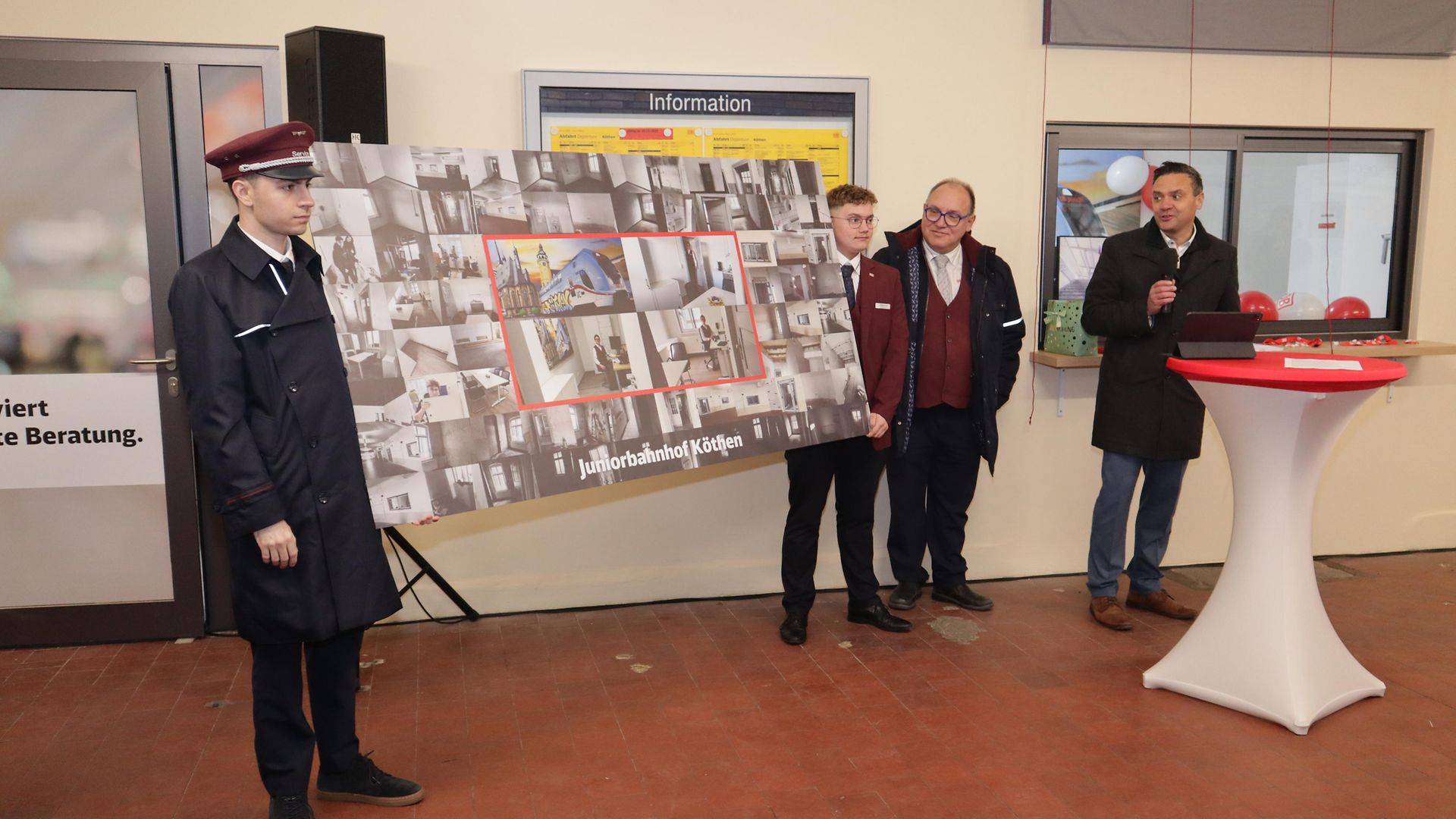 Ältere und jüngere DB-Mitarbeiter präsentieren eine Schautafel im Bahnhof Köthen.