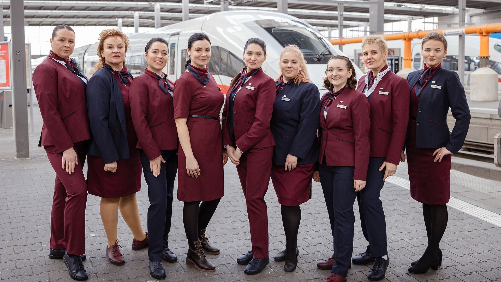 Neun junge Frauen in DB-Unternehmensbekleidung stehen am Bahnsteig und posieren für die Kamera.