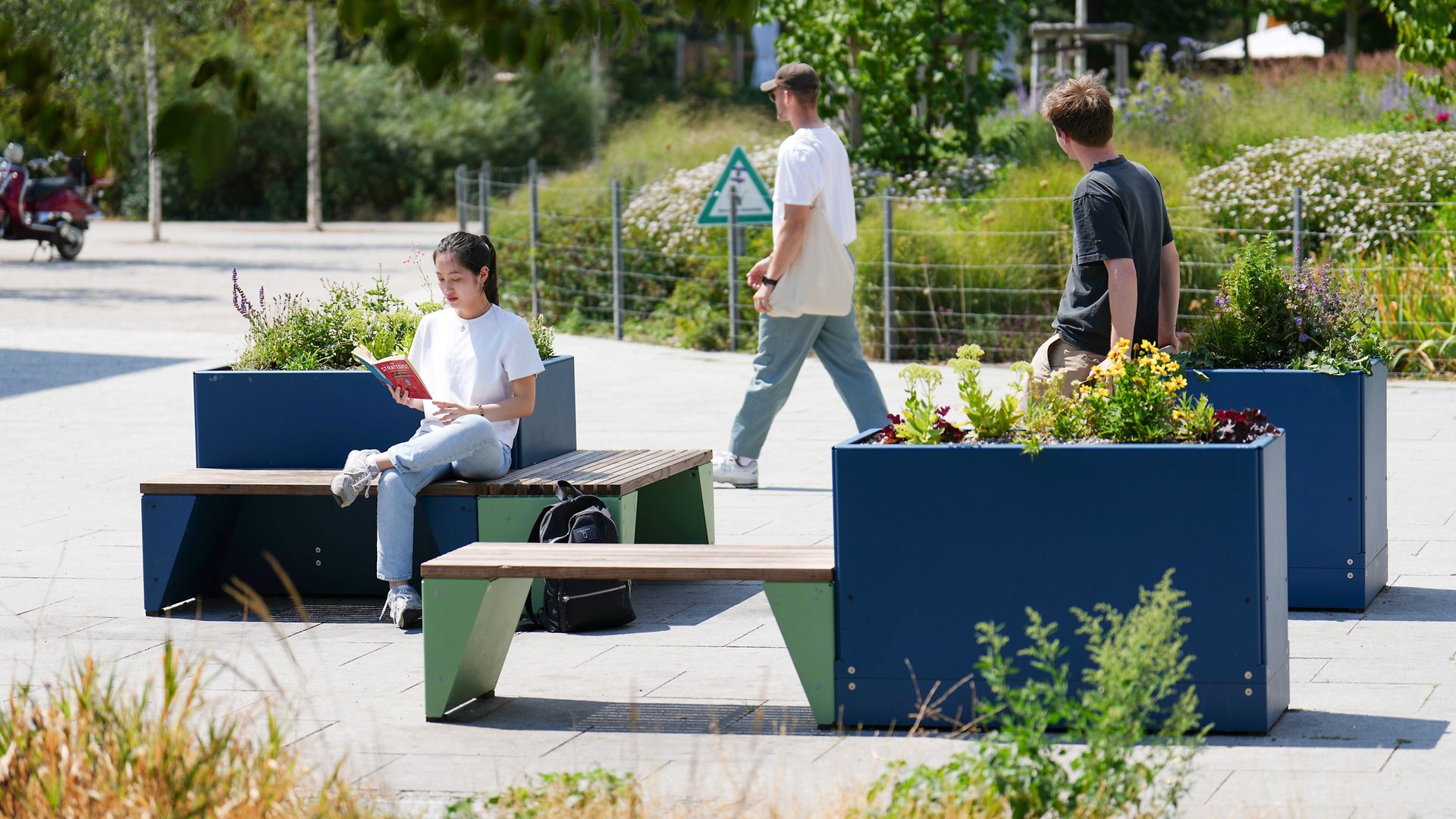 Mehrere Menschen am Bahnhofsvorplatz mit Sitzgelegenheiten und Pflanzen-Laboren