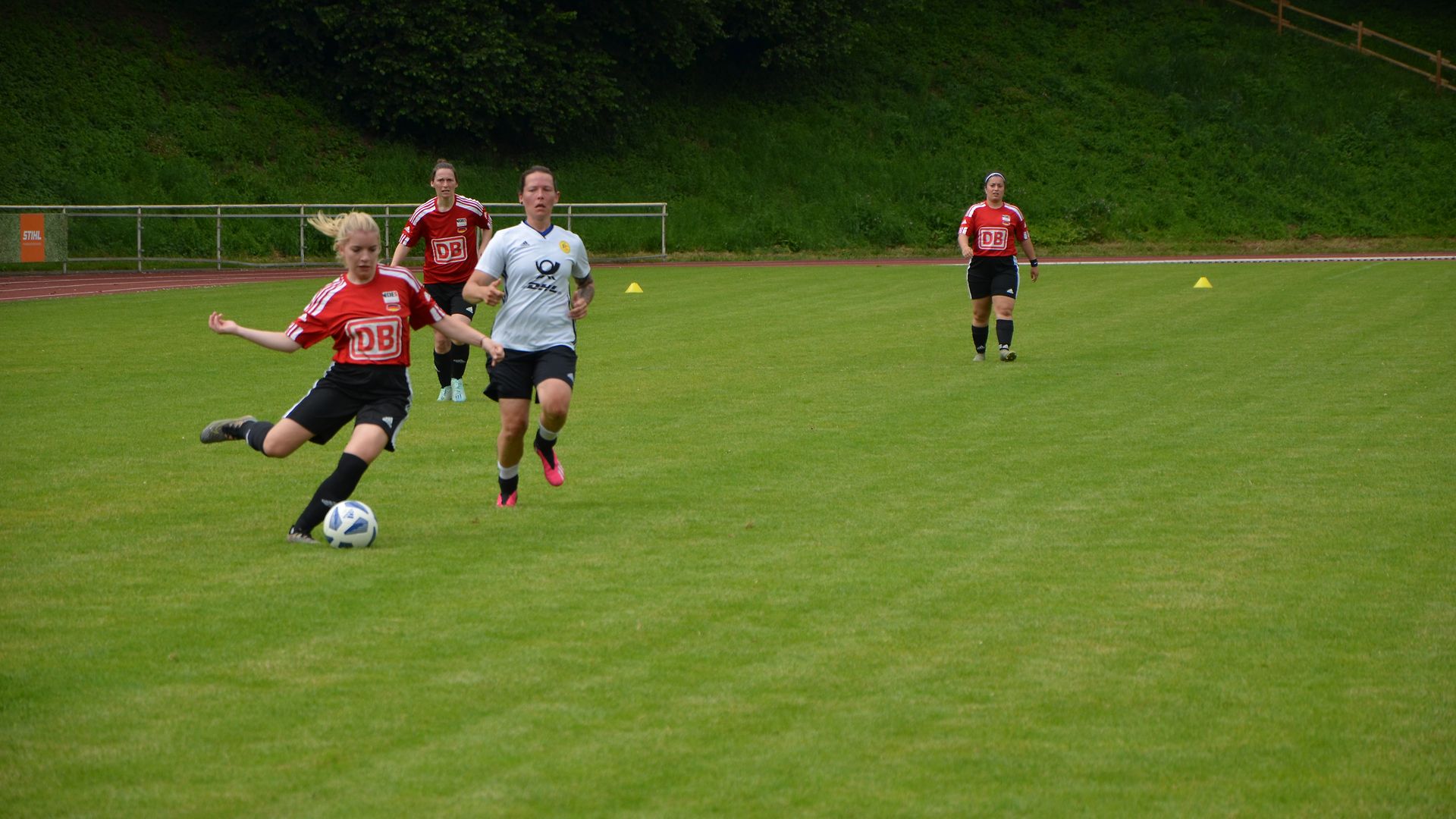 Junge Frauen auf einem Fußballfeld spielen Fußball. Eine Mannschaft trägt Trikots mit DB-Logo.