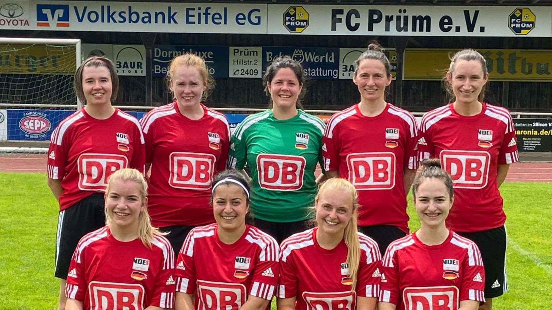 Neun junge Frauen in DB-Trikots posieren als Mannschaft in einem Stadion.
