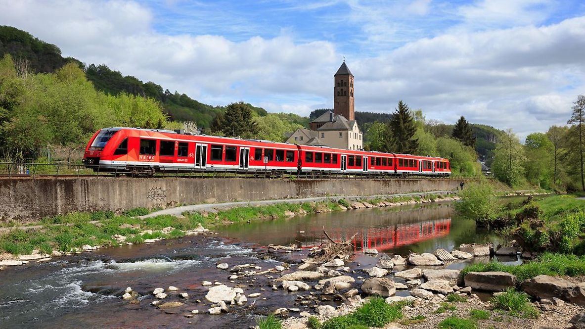 Ein Regionalexpress fährt neben einem Fluss entlang.