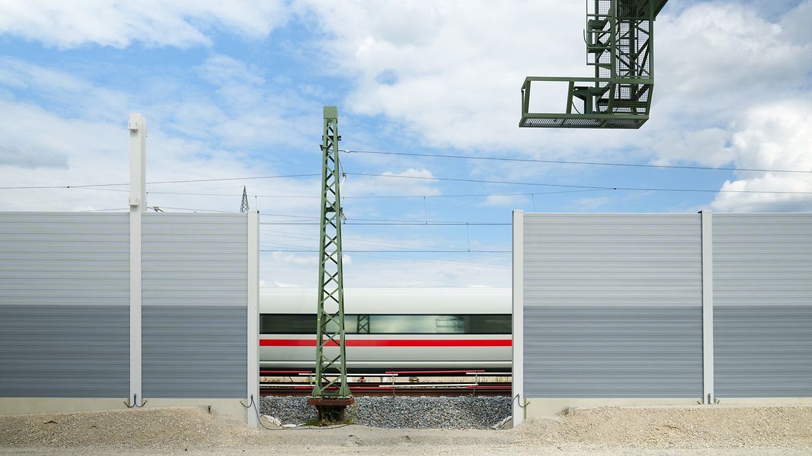 Eine Schallschutzwand an der Bahnstrecke im Bau mit einem vorbeifahrenden Zug